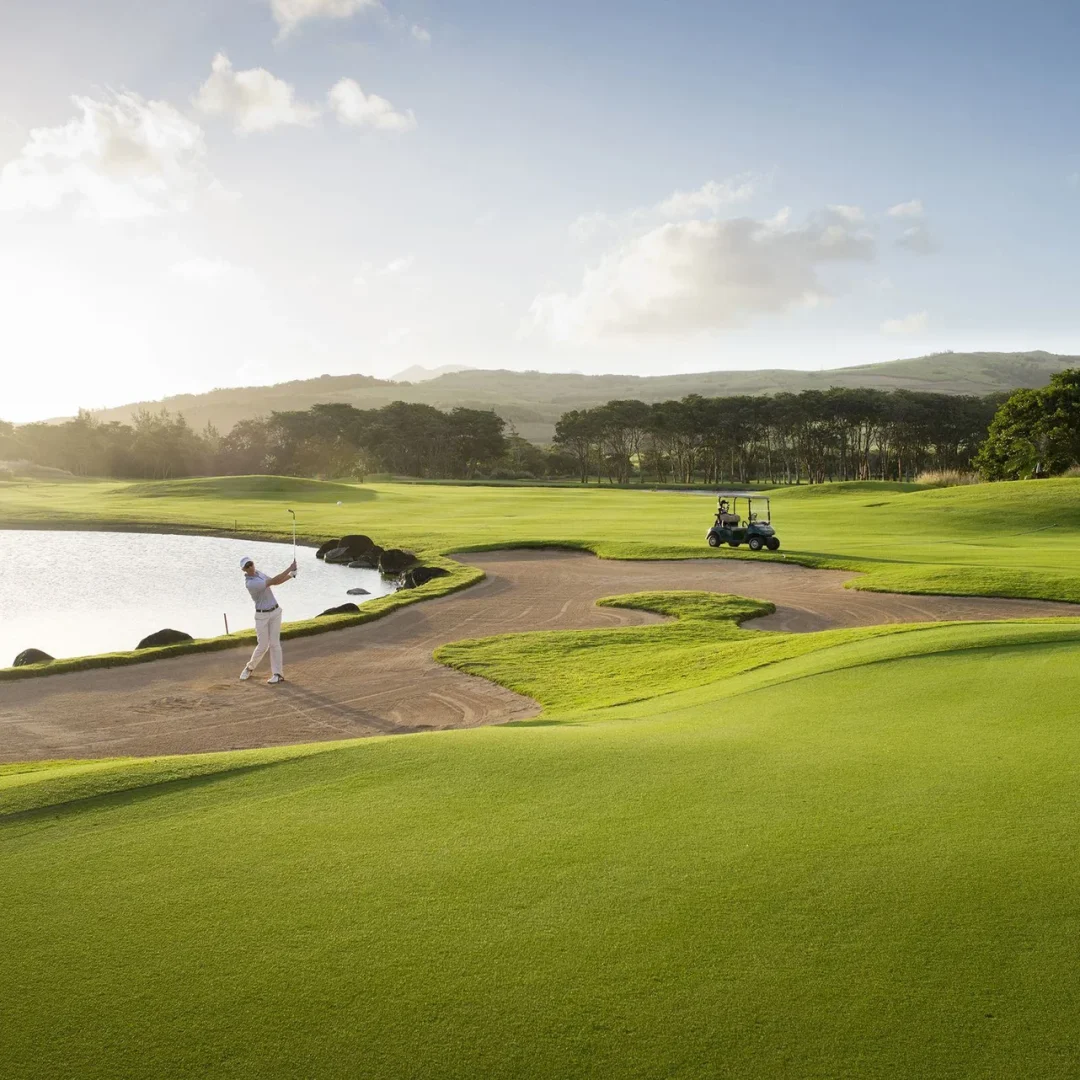 A golfer playing out of a fairway bunker beside the lake at sunrise